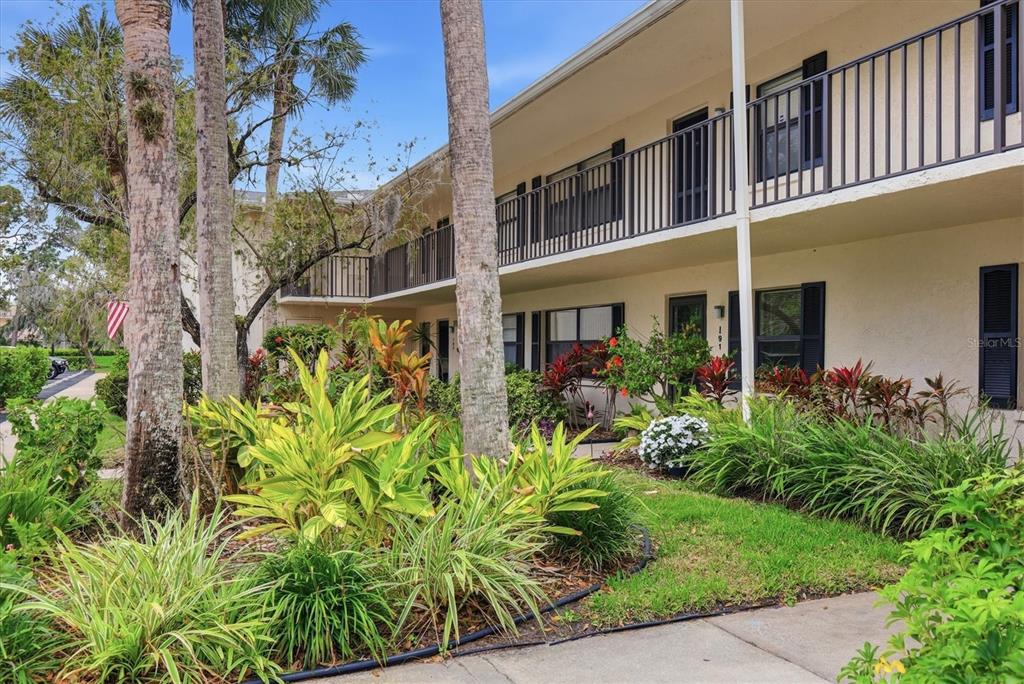 A two-story apartment building exterior features a balcony, palm trees, and landscaped garden beds — 7130 FAIRWAY BEND LANE UNIT 291, SARASOTA, FL