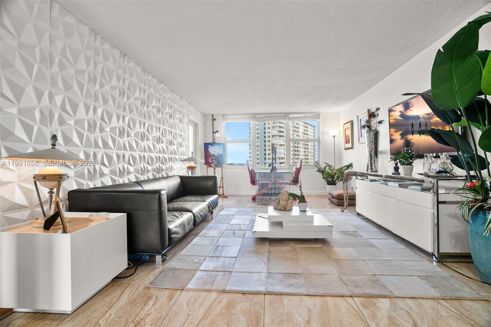 A living room features a textured accent wall, a black leather sofa, and tile flooring — 201 N Ocean Blvd # 509, Pompano Beach FL 33062, POMPANO BEACH, FL