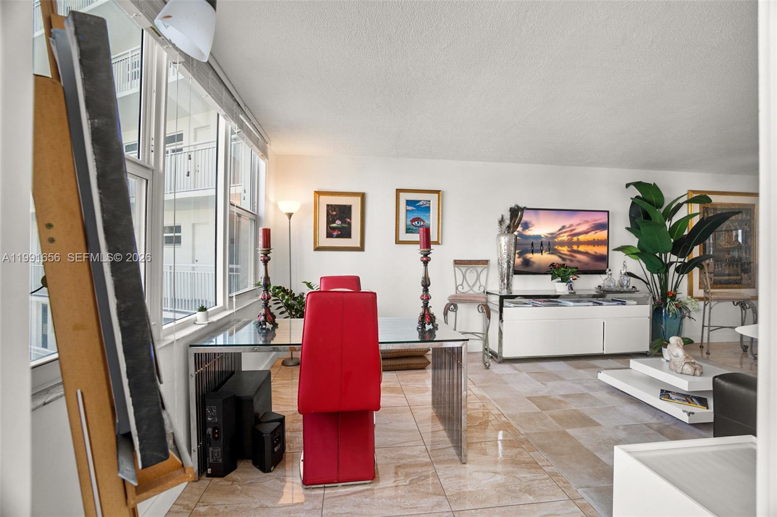 A dining area with a glass table and red chairs sits beside a living room — 201 N Ocean Blvd # 509, Pompano Beach FL 33062, POMPANO BEACH, FL