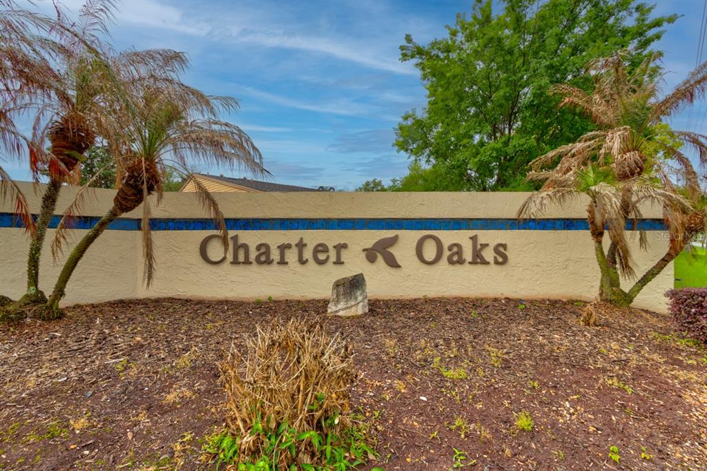 A beige stucco community entrance sign for Charter Oaks stands between two palm trees — 1262 CHARTER OAKS CIRCLE UNIT none, HOLLY HILL, FL