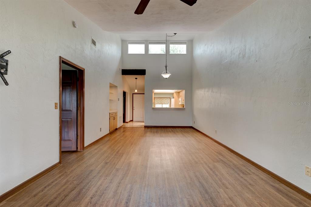 A living room with high ceilings, wood-look flooring, and a pass-through window to the kitchen — 1262 CHARTER OAKS CIRCLE UNIT none, HOLLY HILL, FL