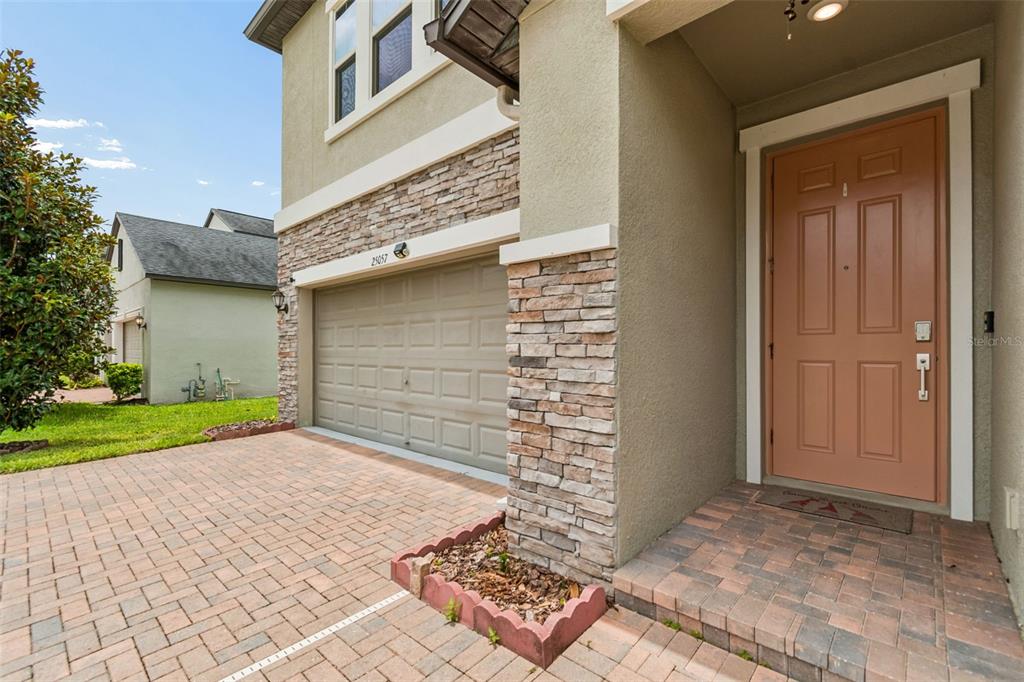 A tan house exterior features a stone-accented garage, a paved driveway, and a front door — 25057 LAMBRUSCO LOOP, LUTZ, FL