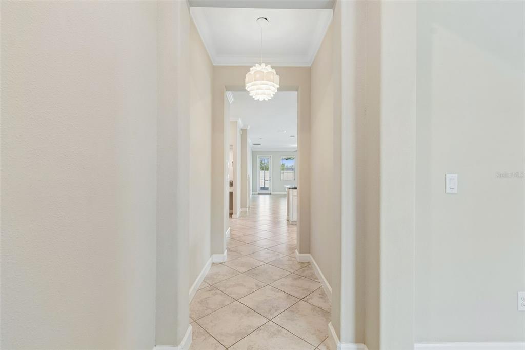 A tiled hallway leads from a foyer toward a bright, open-concept living area — 25057 LAMBRUSCO LOOP, LUTZ, FL