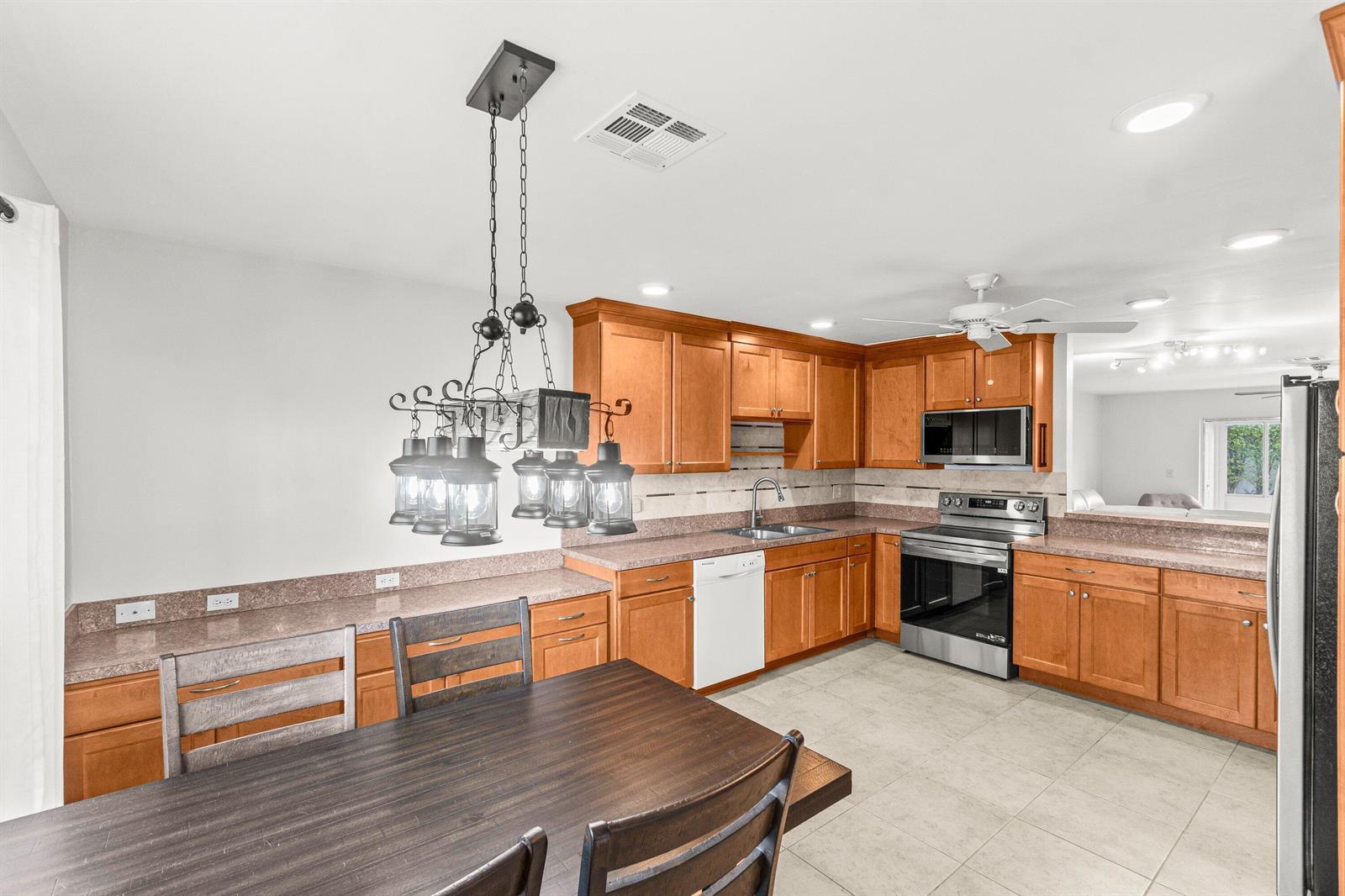 A kitchen features wood cabinets, granite countertops, stainless steel appliances, and a dining area — 5074 Privet Place # B, Delray Beach FL 33484, DELRAY BEACH, FL