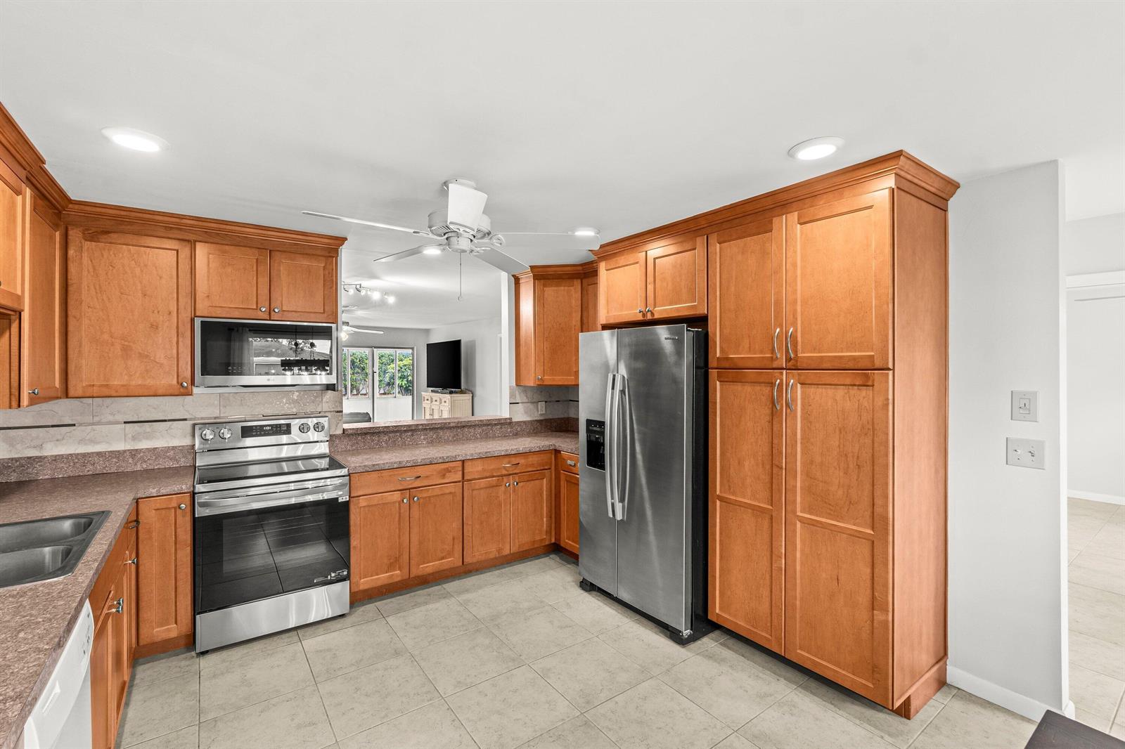 A kitchen features wood cabinets, stainless steel appliances, and a pass-through window to the living area — 5074 Privet Place # B, Delray Beach FL 33484, DELRAY BEACH, FL