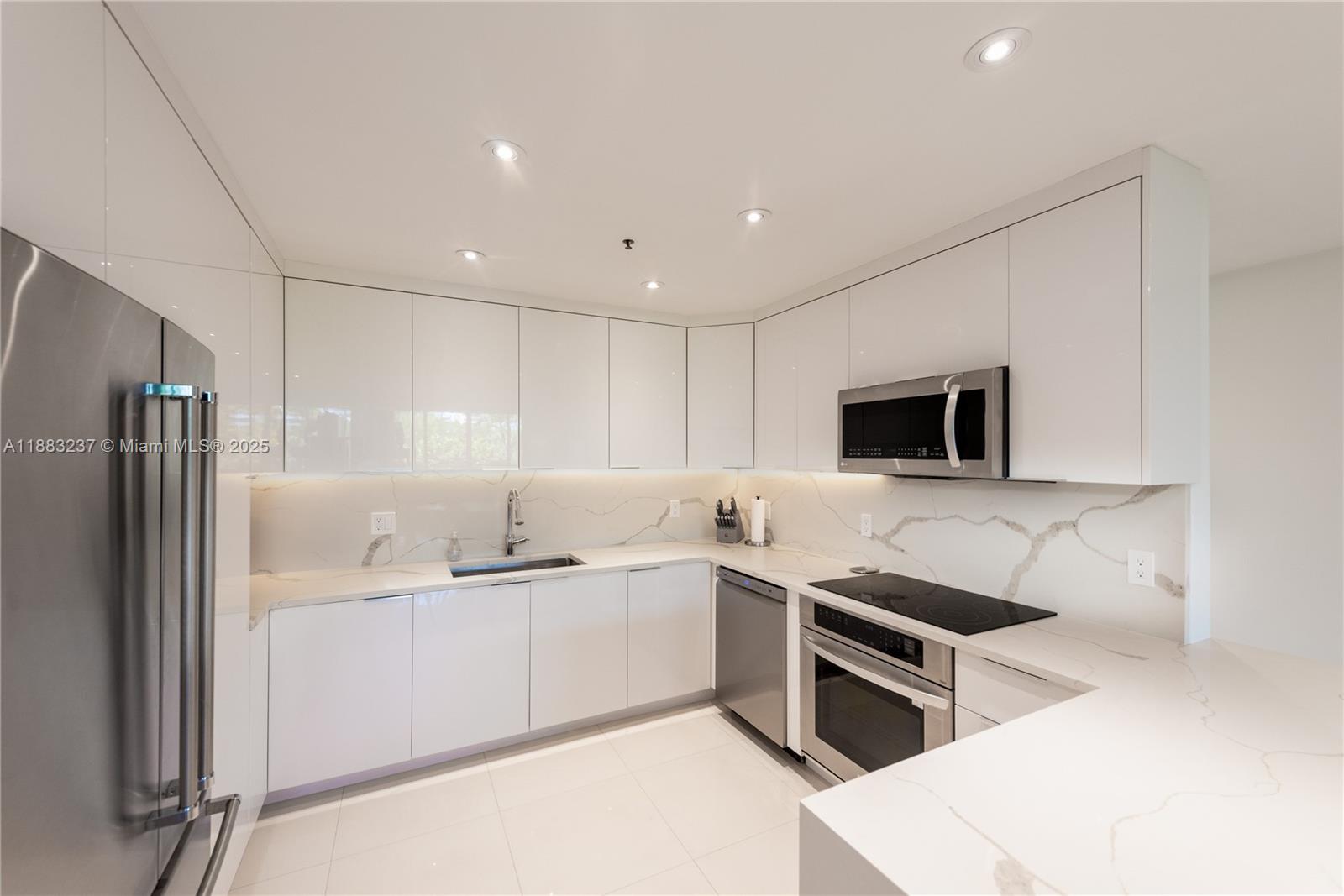 A modern kitchen features white glossy cabinets, stainless steel appliances, and marble-patterned countertops — 251 Crandon Blvd # 227, Key Biscayne FL 33149, KEY BISCAYNE, FL