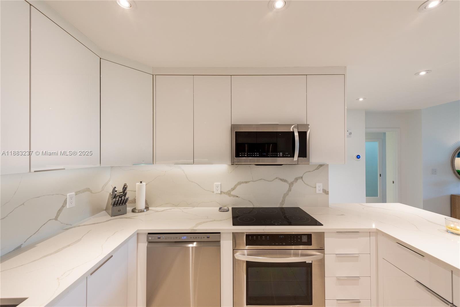 A modern kitchen features white glossy cabinets, stainless steel appliances, and a marble-patterned backsplash — 251 Crandon Blvd # 227, Key Biscayne FL 33149, KEY BISCAYNE, FL