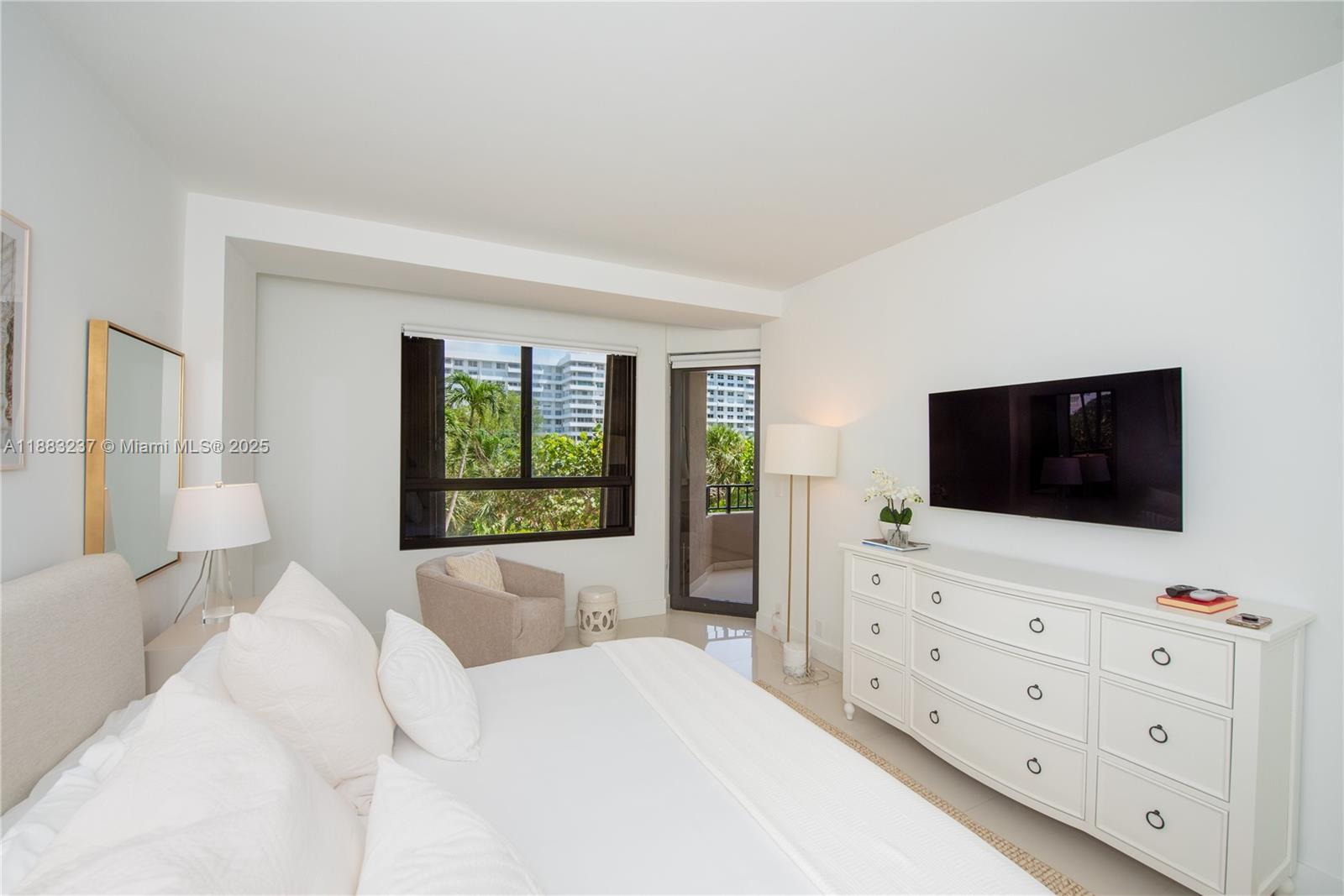 A bright bedroom features a white bed, dresser, wall-mounted television, and a balcony door — 251 Crandon Blvd # 227, Key Biscayne FL 33149, KEY BISCAYNE, FL