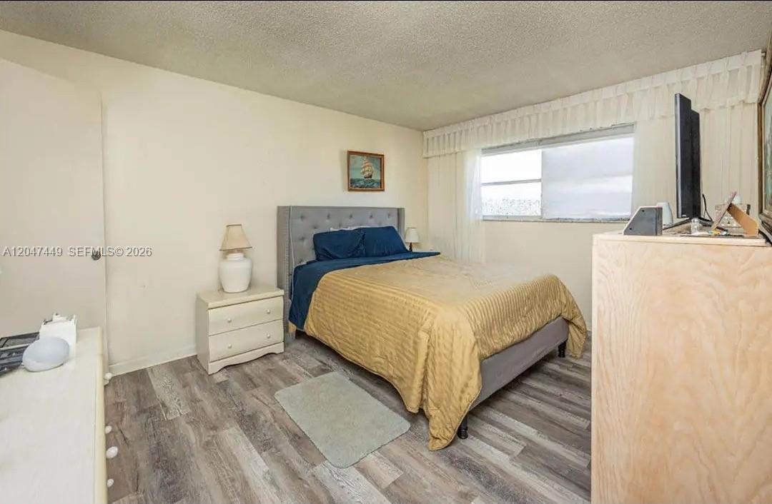 A bedroom with a gray tufted headboard, wood-look flooring, and a window with white curtains — 2615 NE 3rd Ct # 4030, Boynton Beach FL 33435, BOYNTON BEACH, FL