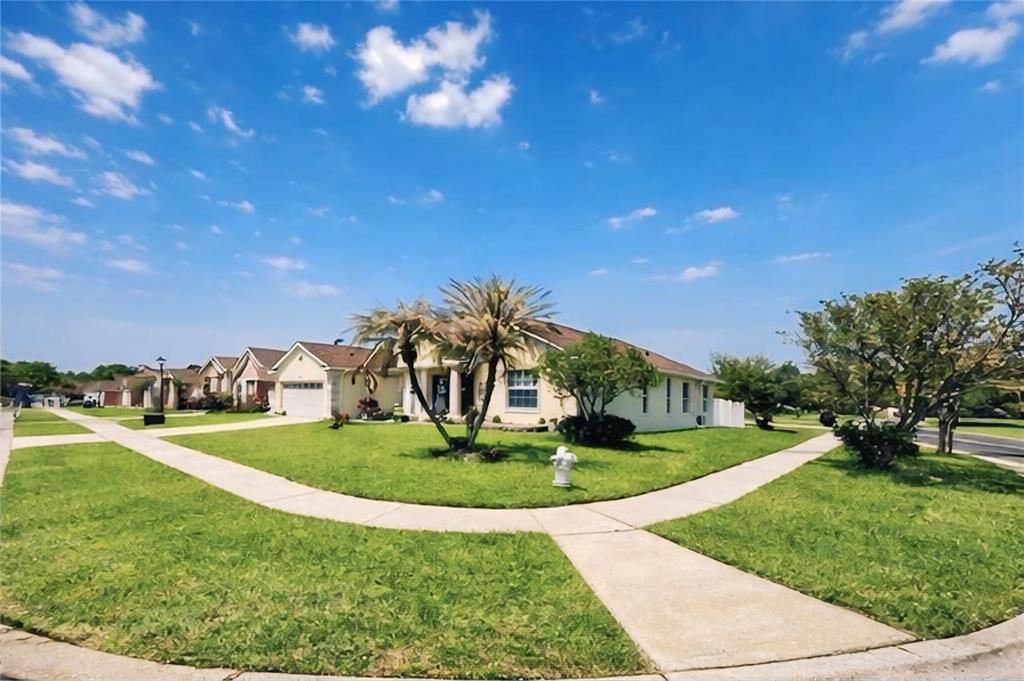 The exterior of a yellow house features a grassy lawn, a patio, and two doors — 2601 GOLD DUST CIRCLE, KISSIMMEE, FL