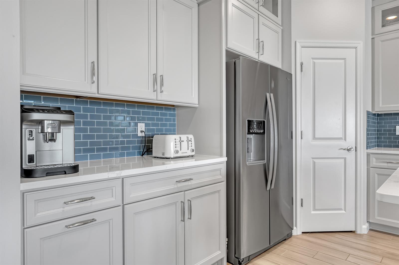 A kitchen features light gray cabinets, blue subway tile backsplash, stainless steel appliances, and countertops — 9774 SW Meridian Way, Stuart FL 34997, STUART, FL