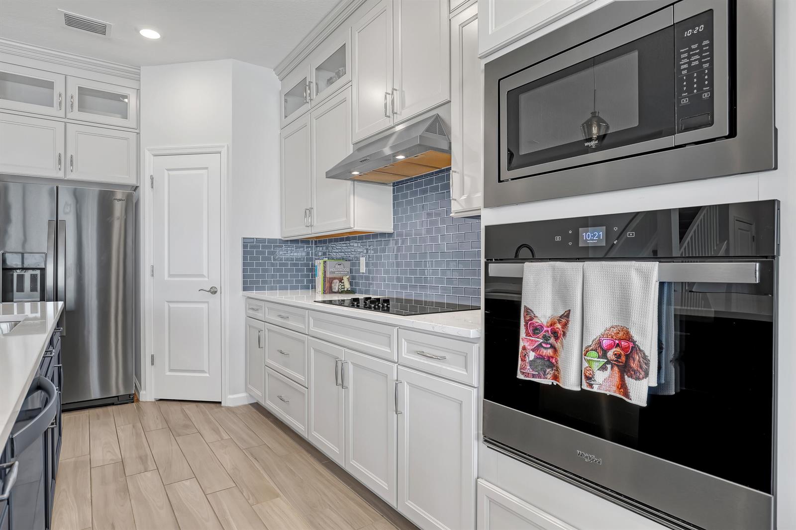 A kitchen features white cabinetry, stainless steel appliances, a blue subway tile backsplash, and wood-look flooring — 9774 SW Meridian Way, Stuart FL 34997, STUART, FL