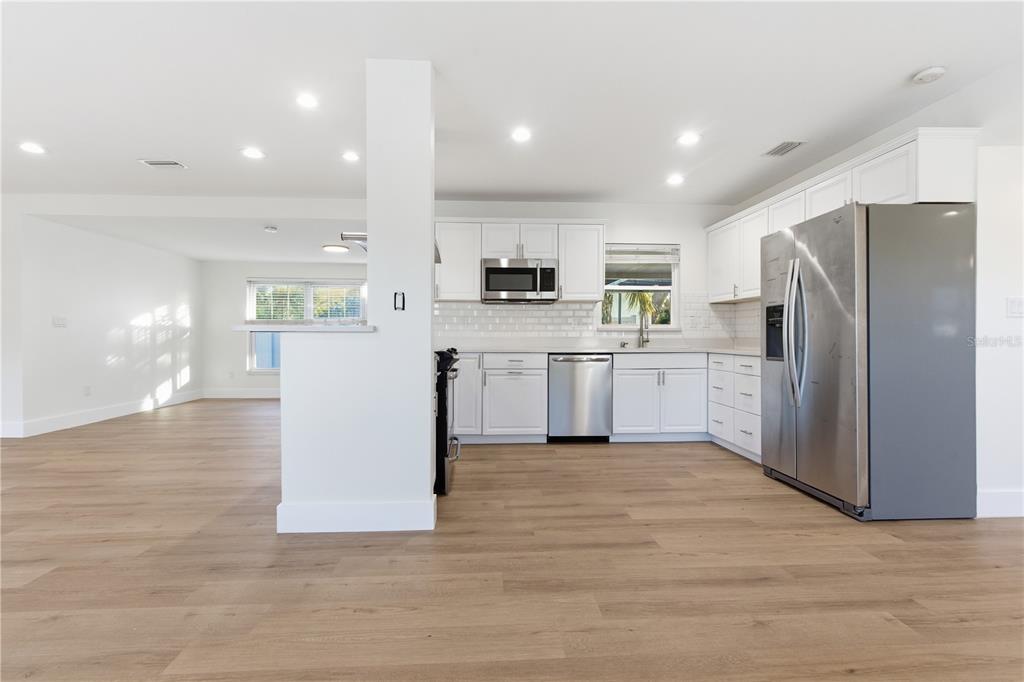 A modern kitchen features white cabinets, stainless steel appliances, and light wood-look flooring — 327 SUNNY LANE, BELLEAIR, FL