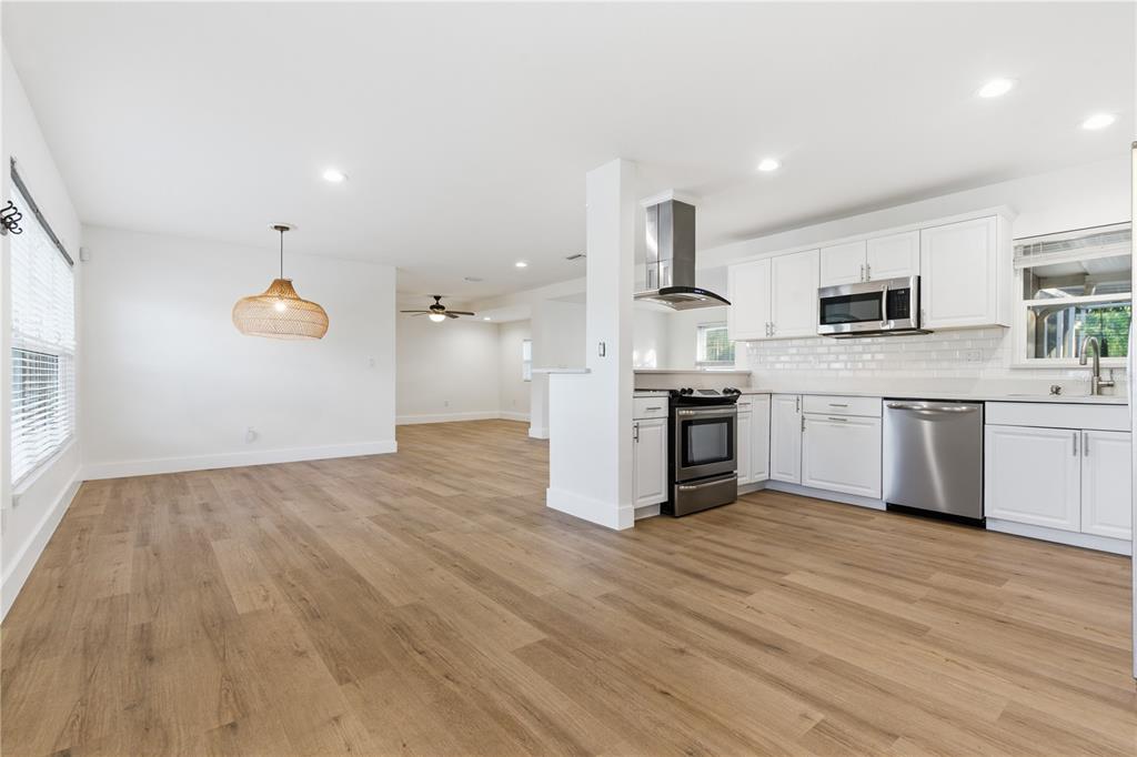 An open-concept kitchen and dining area features white cabinetry, stainless steel appliances, and wood flooring — 327 SUNNY LANE, BELLEAIR, FL