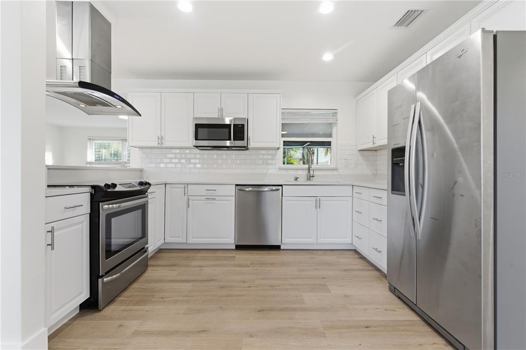 A kitchen features white cabinets, stainless steel appliances, a subway tile backsplash, and wood flooring — 327 SUNNY LANE, BELLEAIR, FL