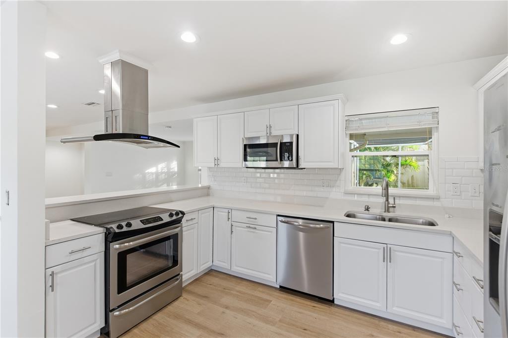 A modern kitchen features white cabinets, stainless steel appliances, a subway tile backsplash, and wood flooring — 327 SUNNY LANE, BELLEAIR, FL