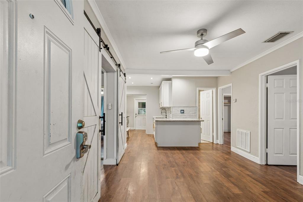 An interior view shows a kitchen with white cabinets and wood flooring near an entryway — 3521 74TH AVENUE N, PINELLAS PARK, FL