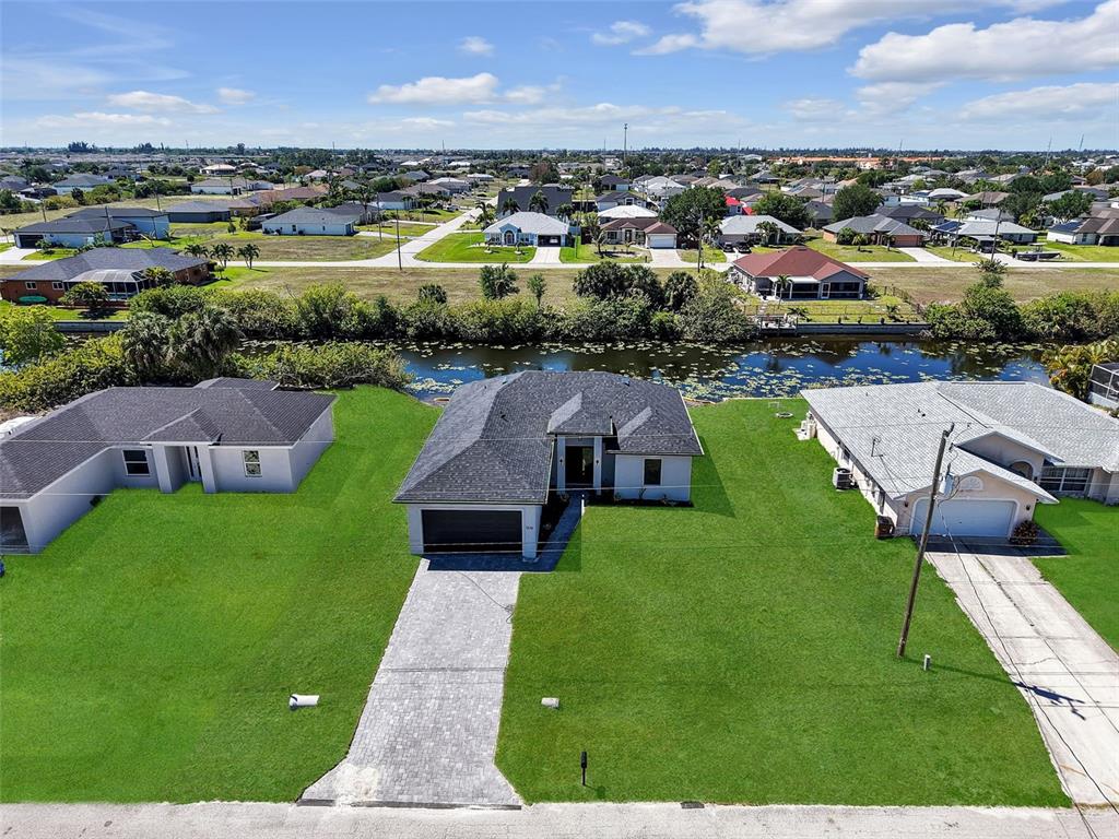 An aerial view shows a single-story house with a gray roof and paved driveway — 1310 NW 11TH TERRACE, CAPE CORAL, FL