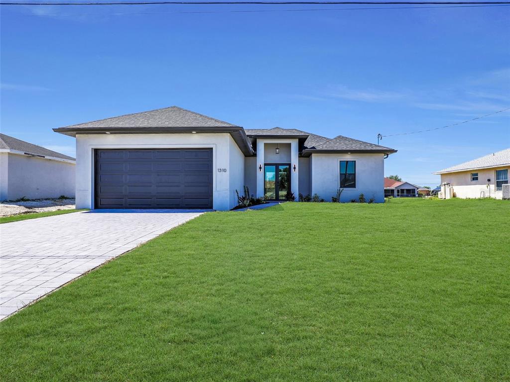 A single-story house with a two-car garage, white stucco exterior, and a paved driveway — 1310 NW 11TH TERRACE, CAPE CORAL, FL