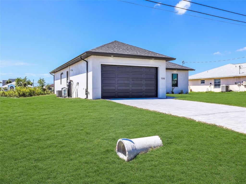 A single-story house with a white stucco exterior and a dark garage door — 1310 NW 11TH TERRACE, CAPE CORAL, FL