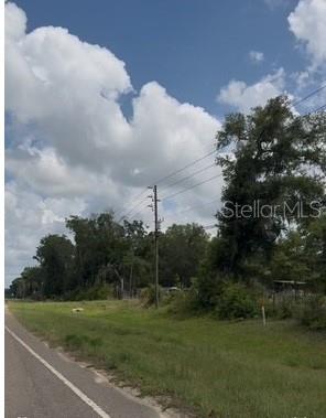 A paved road runs alongside a grassy field with trees and utility poles under a sky — 17297 PONCE DE LEON BOULEVARD, BROOKSVILLE, FL
