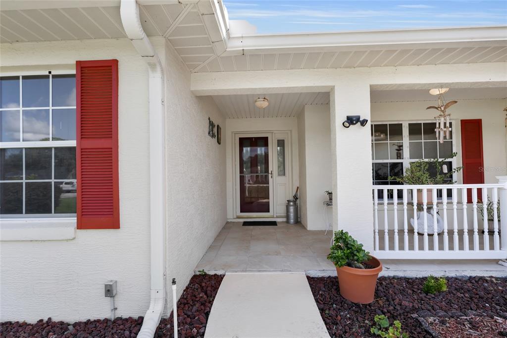 A covered front porch with a white railing, red shutters, and a glass storm door — 5193 SW 110TH PLACE, OCALA, FL