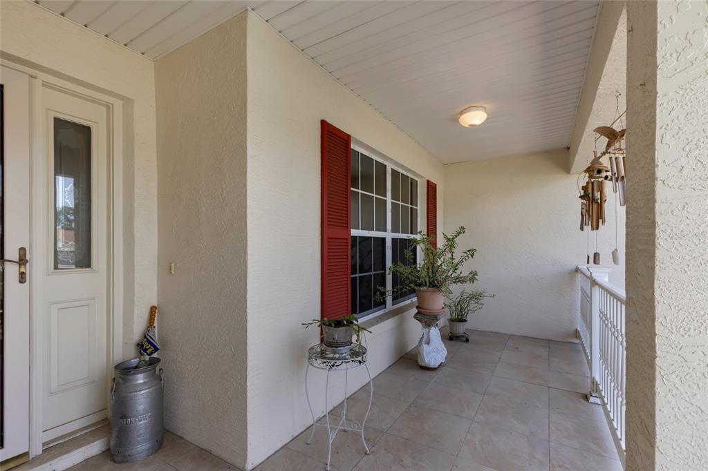 A covered outdoor porch features tiled flooring, a white door, and a window with red shutters — 5193 SW 110TH PLACE, OCALA, FL