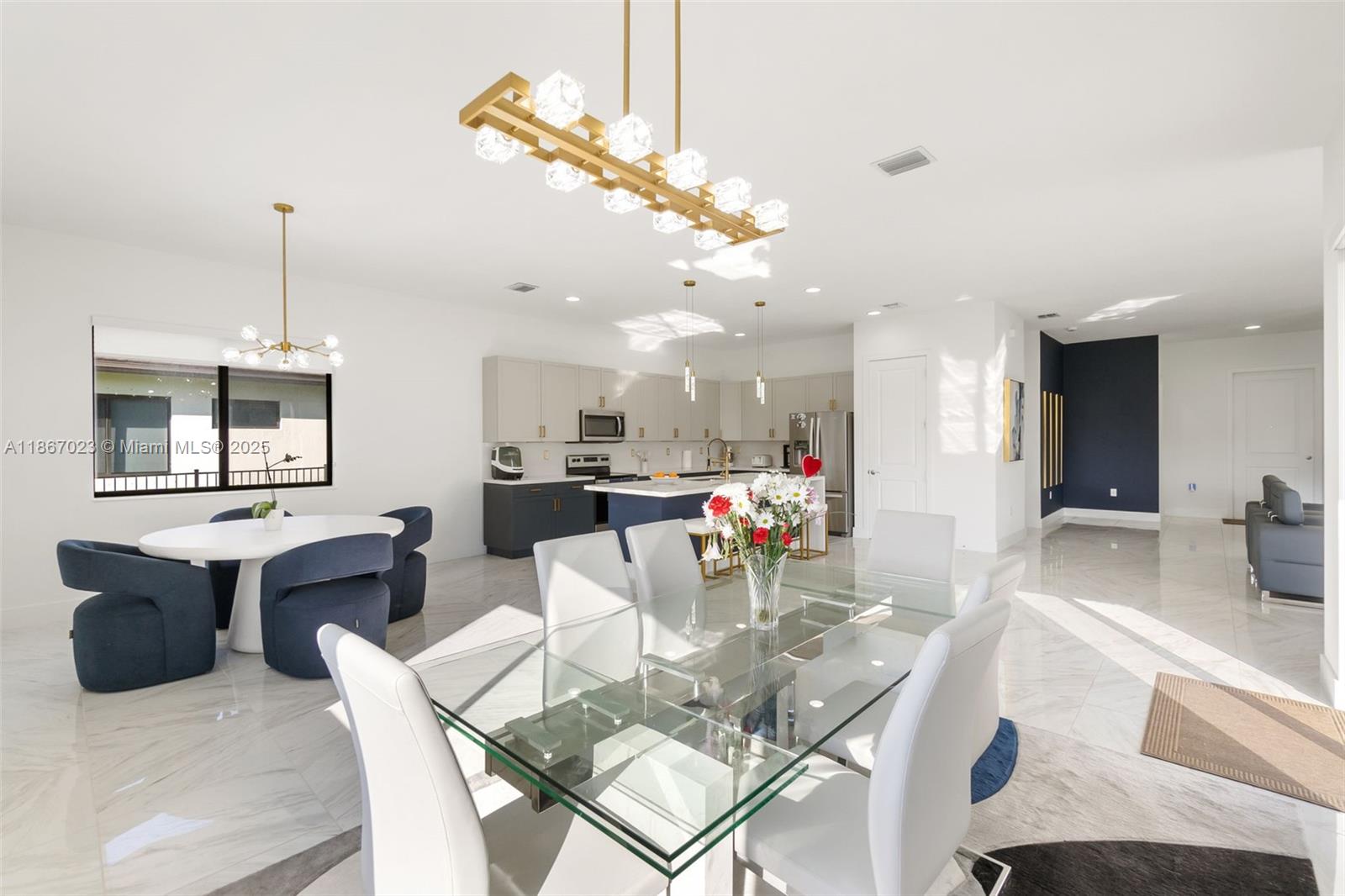 An open-concept dining and kitchen area features white marble floors, modern lighting, and blue accents — 4948 Gambero Way, Ave Maria FL 34142, AVE MARIA, FL