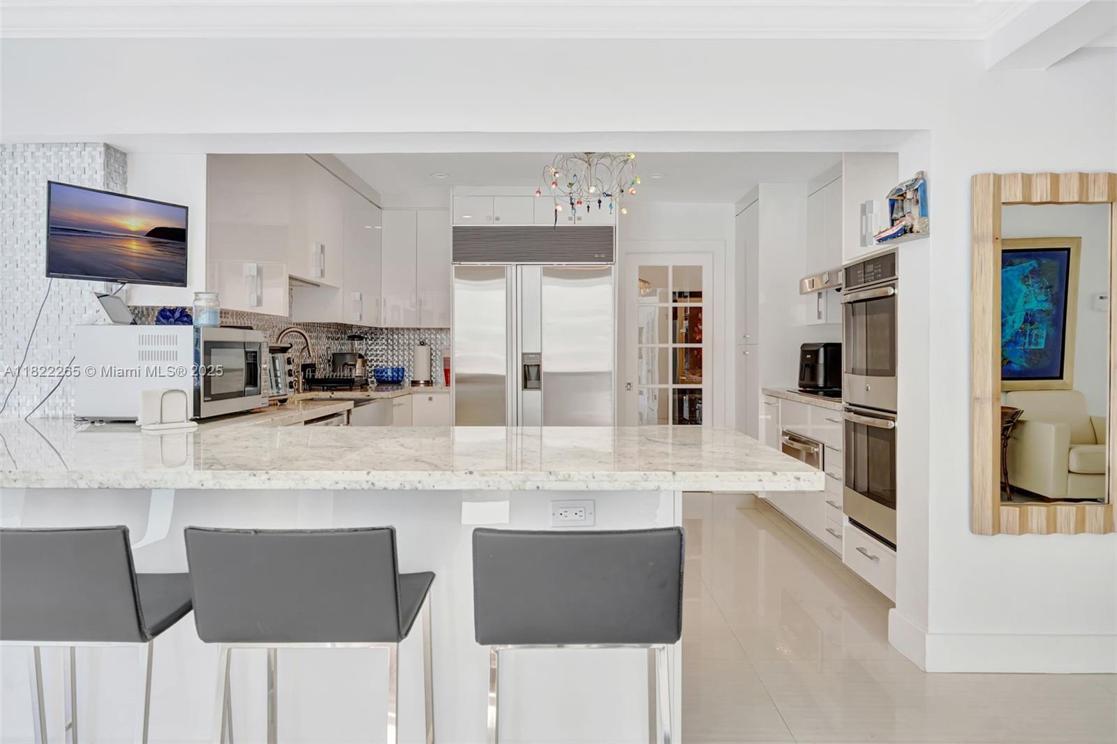 A modern white kitchen features a marble island, stainless steel appliances, and three bar stools — 11230 SW 69th Ct, Pinecrest FL 33156, PINECREST, FL