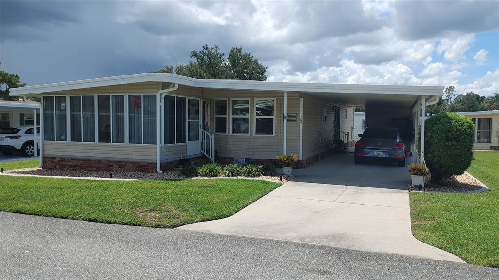 A single-story manufactured home with a screened-in porch, attached carport, and a concrete driveway — 104 CALADIUM STREET, LEESBURG, FL