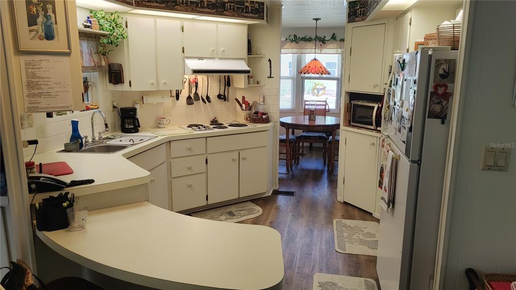 A kitchen with white cabinets, laminate countertops, and a dining area in the background — 104 CALADIUM STREET, LEESBURG, FL