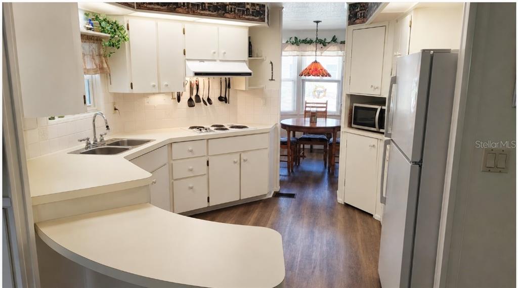 A kitchen with white cabinets, laminate countertops, a white refrigerator, and an adjacent dining area — 104 CALADIUM STREET, LEESBURG, FL
