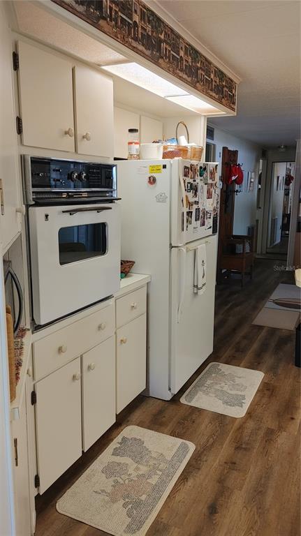 A kitchen features white cabinets, a built-in wall oven, a refrigerator, and wood-look flooring — 104 CALADIUM STREET, LEESBURG, FL