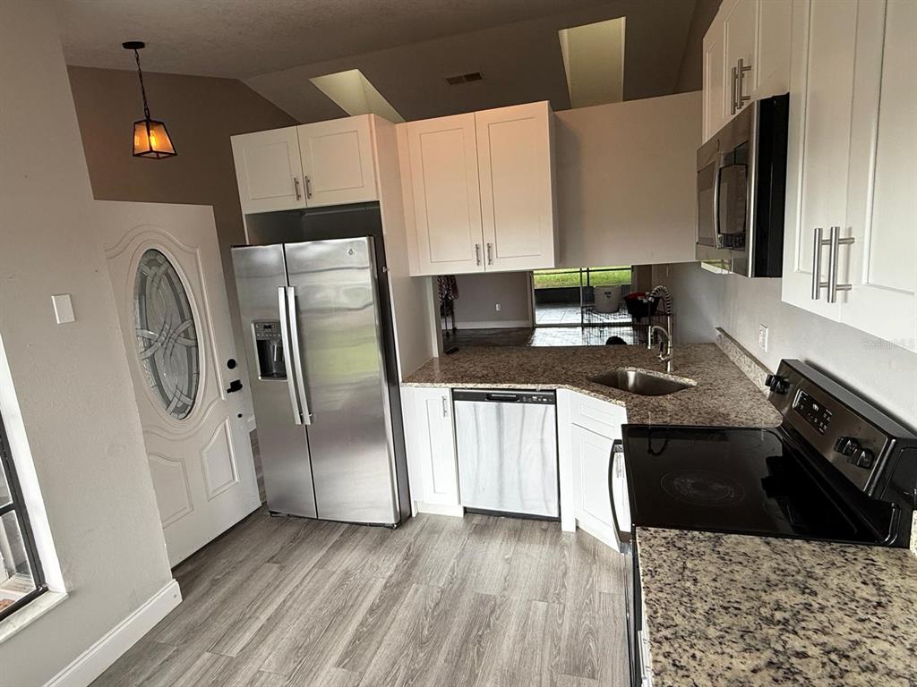 A kitchen features white cabinets, stainless steel appliances, granite countertops, and wood-look flooring — 3010 GALAXY STREET, DELTONA, FL