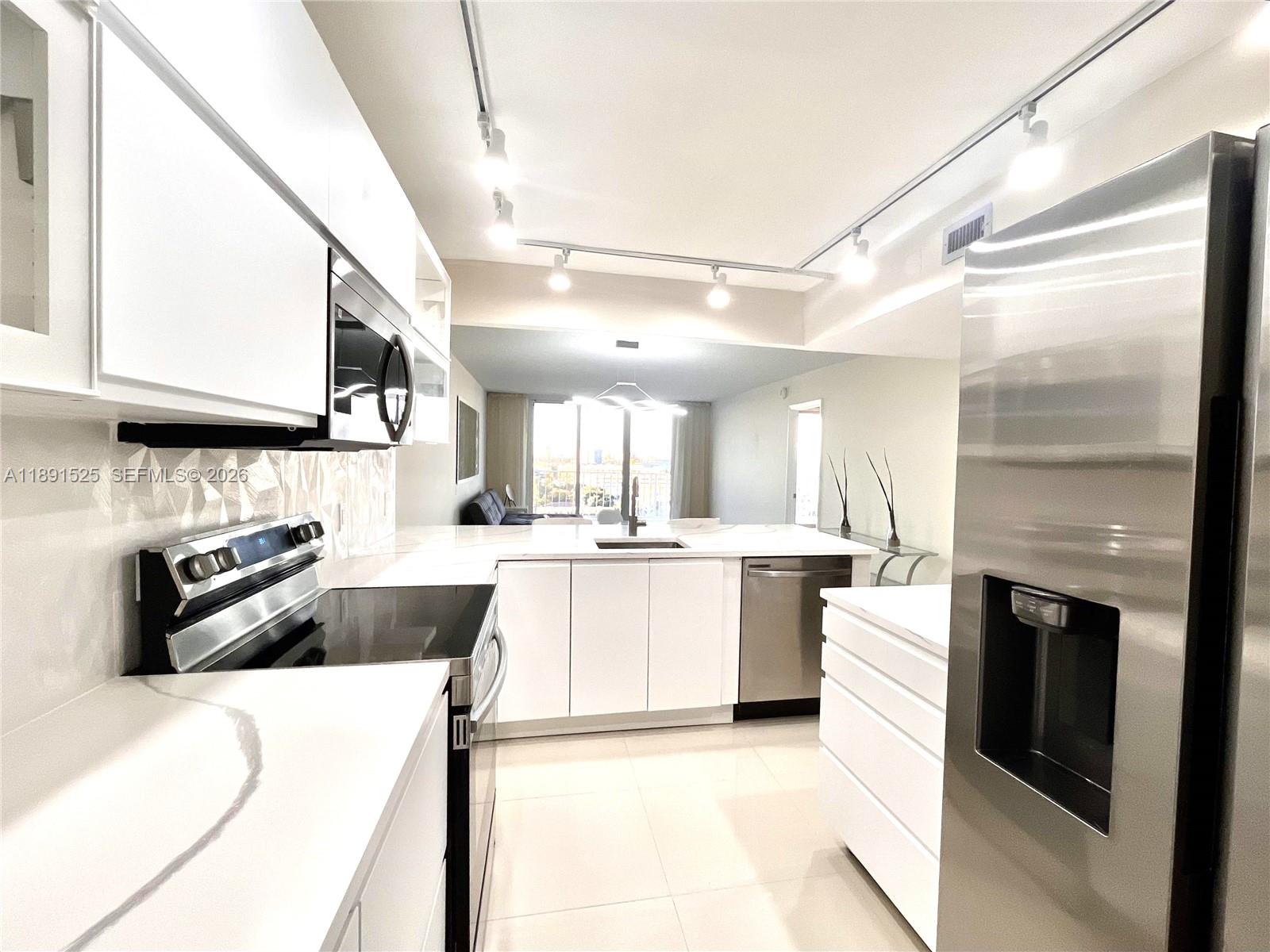 A modern kitchen features white cabinetry, stainless steel appliances, and a central island with sink — 800 SE 20th Ave # 1109, Deerfield Beach FL 33441, DEERFIELD BEACH, FL