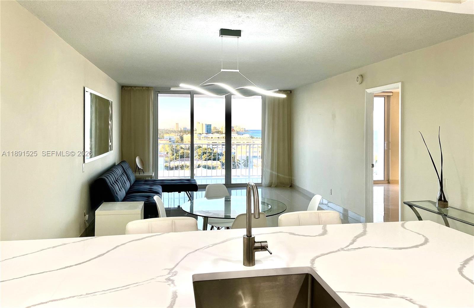 A kitchen island with a marble countertop overlooks a living area with a balcony view — 800 SE 20th Ave # 1109, Deerfield Beach FL 33441, DEERFIELD BEACH, FL