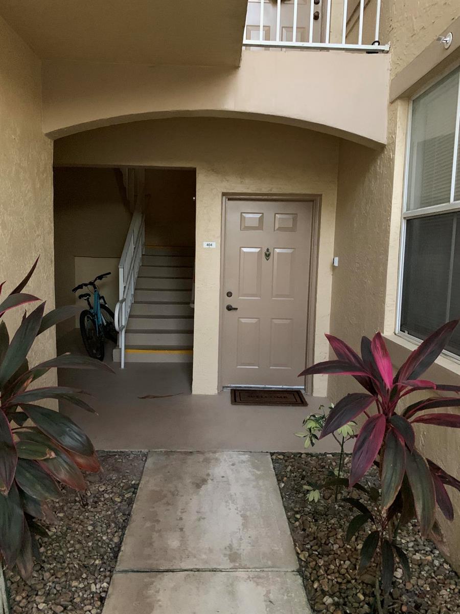 An exterior view of a residential building entrance featuring a tan door labeled 404 — 2080 Greenview Shores Boulevard # 404, FL, FL