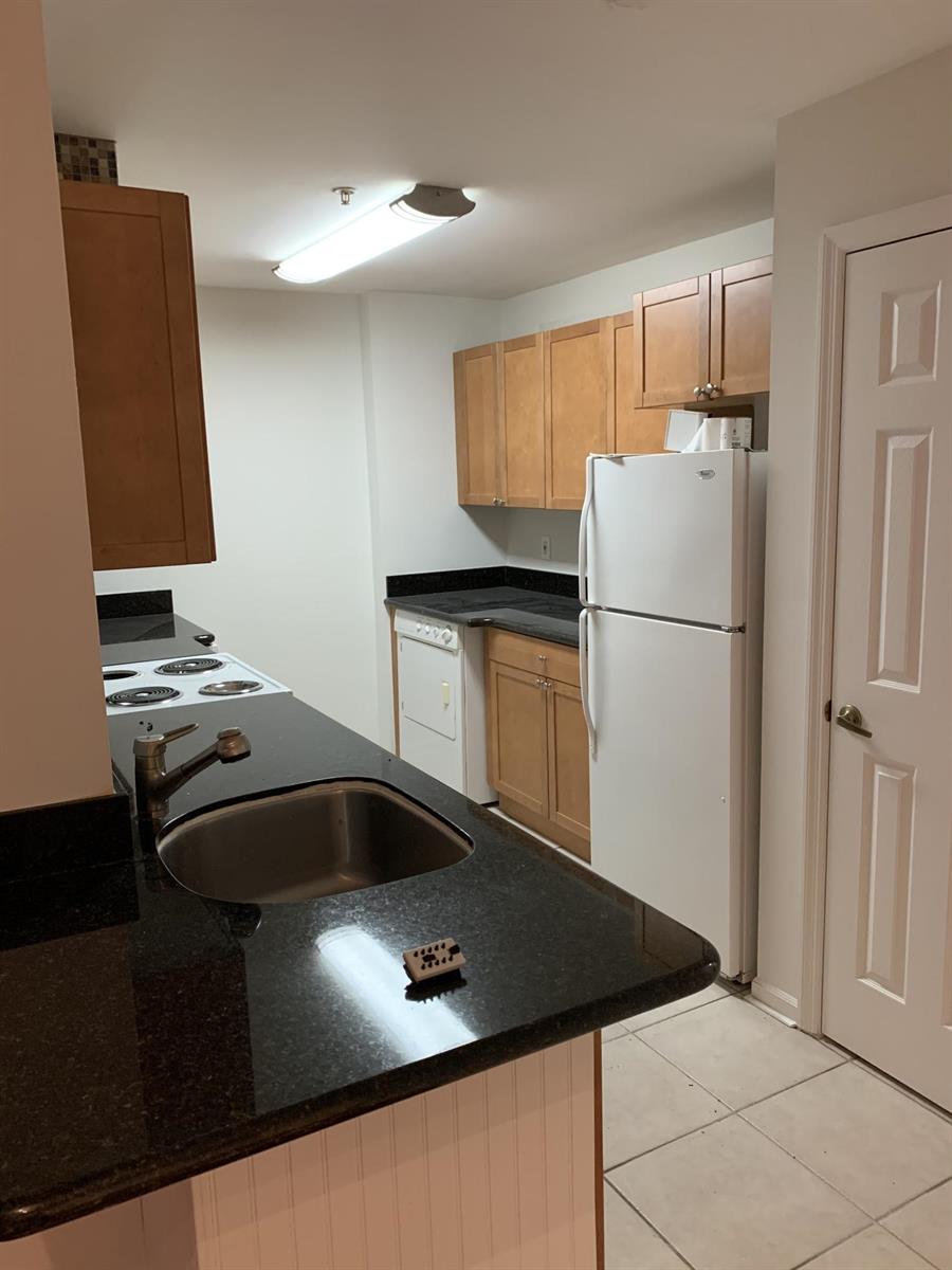 A kitchen features light wood cabinets, black countertops, a white refrigerator, and a stainless sink — 2080 Greenview Shores Boulevard # 404, FL, FL