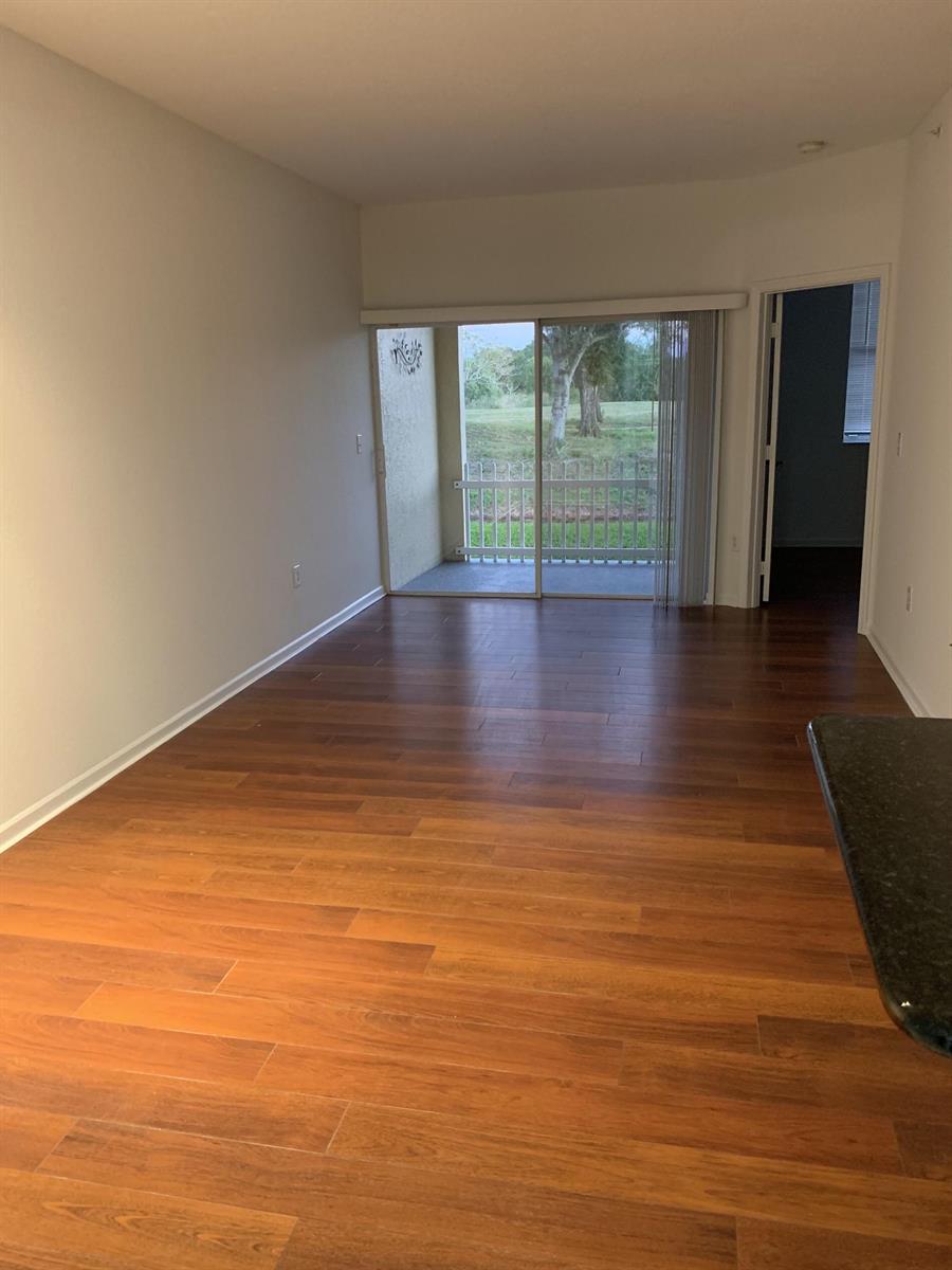 An empty living room with wood-look flooring, a sliding glass door, and a balcony view — 2080 Greenview Shores Boulevard # 404, FL, FL