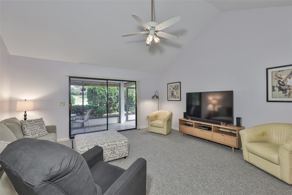 A living room with gray carpet, a vaulted ceiling, a ceiling fan, and sliding glass doors — 1305 SPRY COURT, SUN CITY CENTER, FL