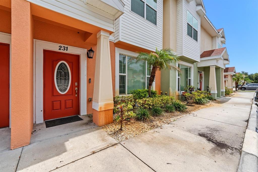 The exterior of a multi-story townhouse features a red front door and a small garden — 231 ALEXANDER WOODS DRIVE, PLANT CITY, FL