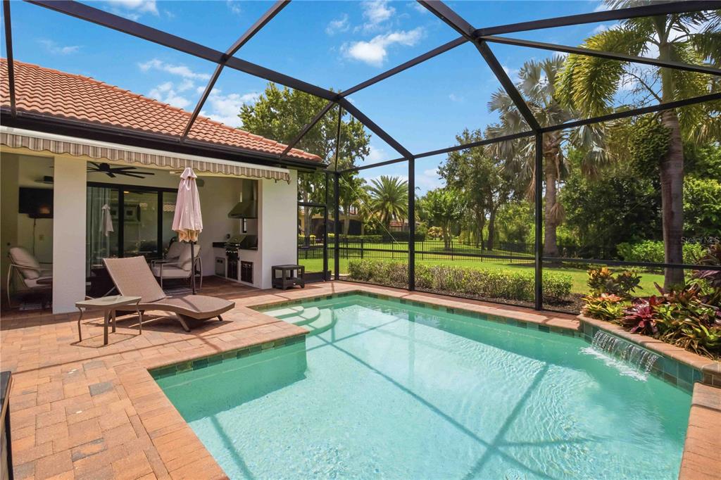 A screened-in patio features a swimming pool with a waterfall and an outdoor kitchen area — 15414 LEVEN LINKS PLACE, BRADENTON, FL