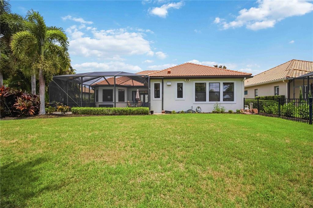 The backyard of a house features a screened-in patio, a lawn, and a metal fence — 15414 LEVEN LINKS PLACE, BRADENTON, FL
