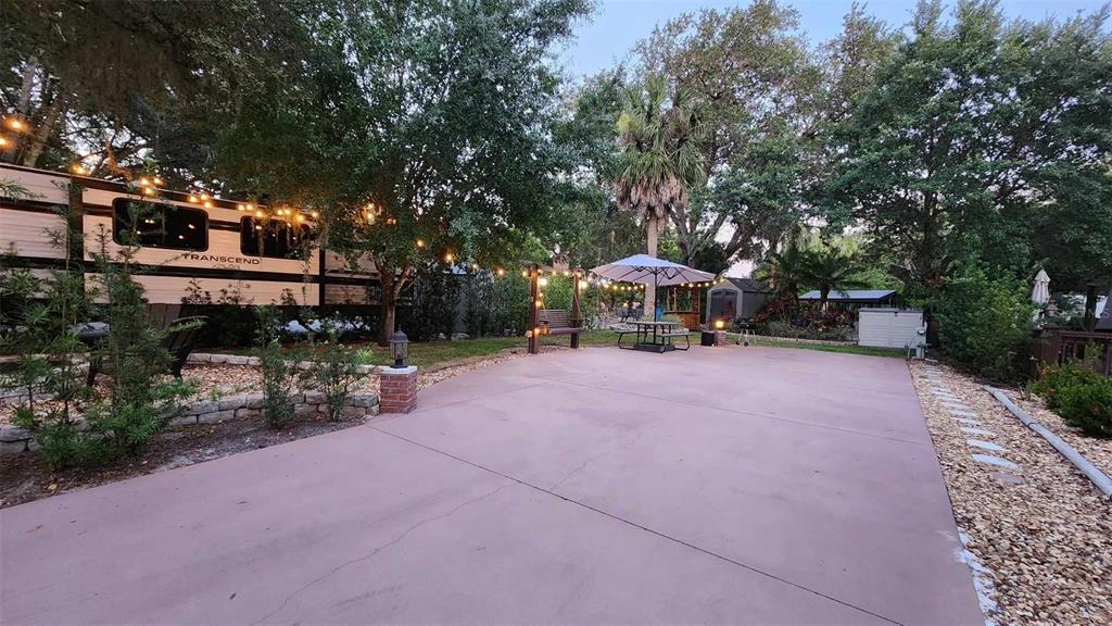 A paved patio area features a parked travel trailer, a swing, and an outdoor umbrella — 187 LONGHORN DRIVE, LAKE WALES, FL