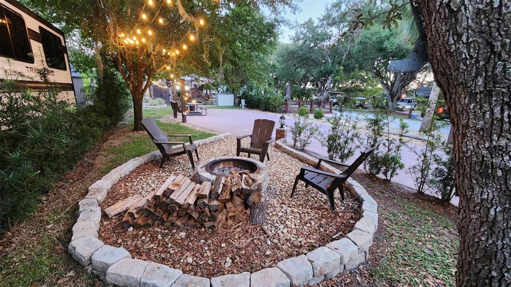 A circular stone fire pit area with three chairs and a wood pile outdoors — 187 LONGHORN DRIVE, LAKE WALES, FL
