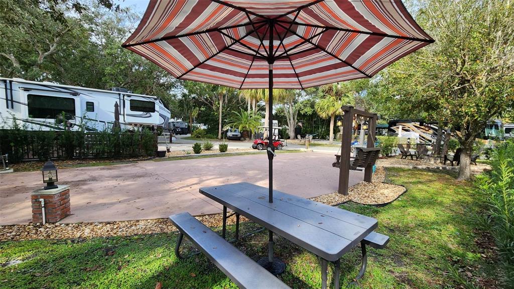 A picnic table with a striped umbrella sits on a patio next to an RV — 187 LONGHORN DRIVE, LAKE WALES, FL