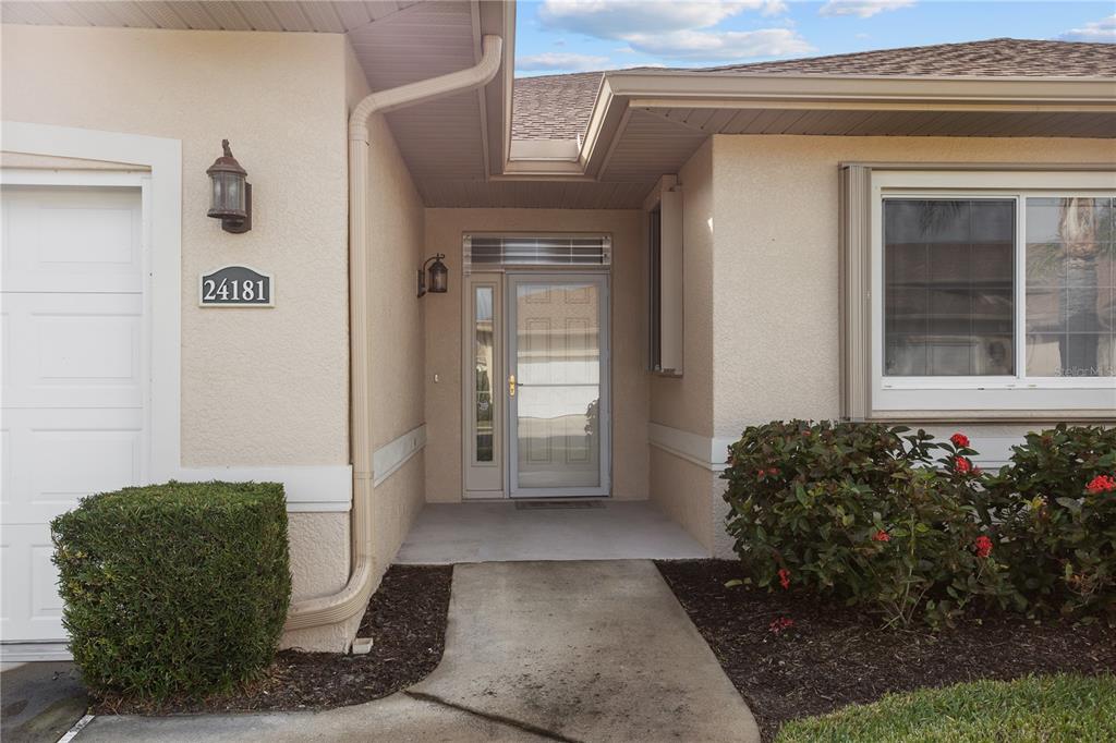 A beige house exterior features a front door with a sidelight and a concrete walkway — 24181 GREEN HERON DRIVE UNIT 84, PUNTA GORDA, FL
