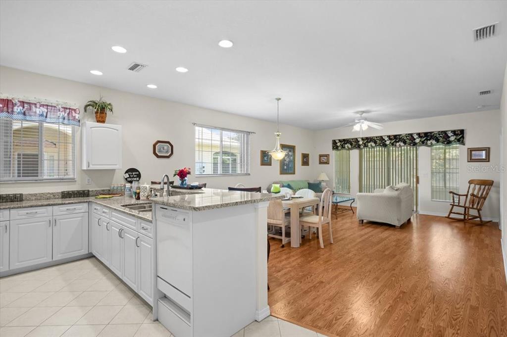 A kitchen with white cabinets and granite countertops opens into a living and dining area — 24181 GREEN HERON DRIVE UNIT 84, PUNTA GORDA, FL
