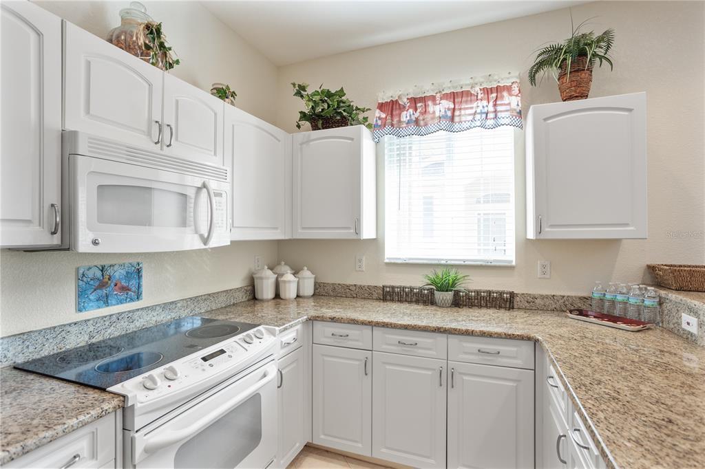 A kitchen features white cabinets, granite countertops, a glass-top stove, and a window with valance — 24181 GREEN HERON DRIVE UNIT 84, PUNTA GORDA, FL