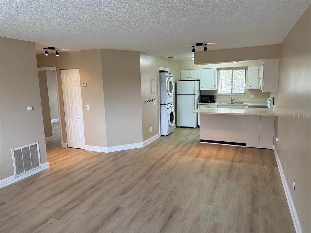 An open-concept living area features light wood-look flooring, a kitchen with white cabinets, and laundry — 7340 SWALLOW RUN UNIT 7340, WINTER PARK, FL